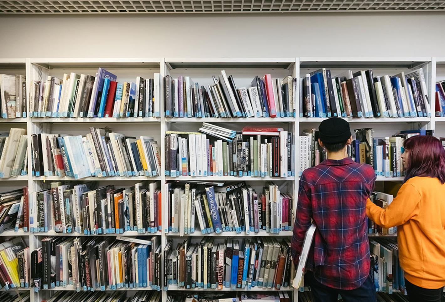 Two students look at books in a library