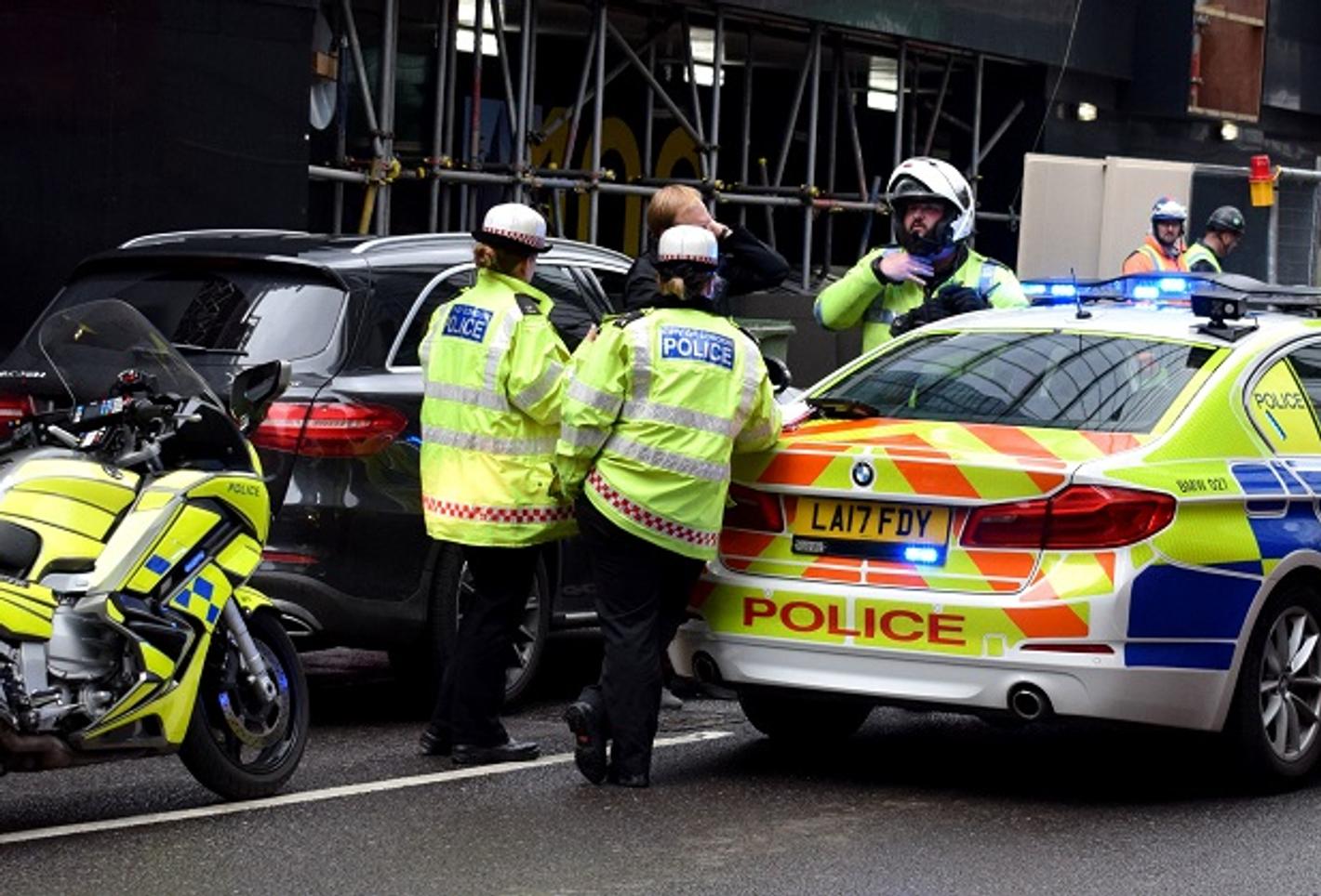 Three law enforcement officers and a police car on the street.