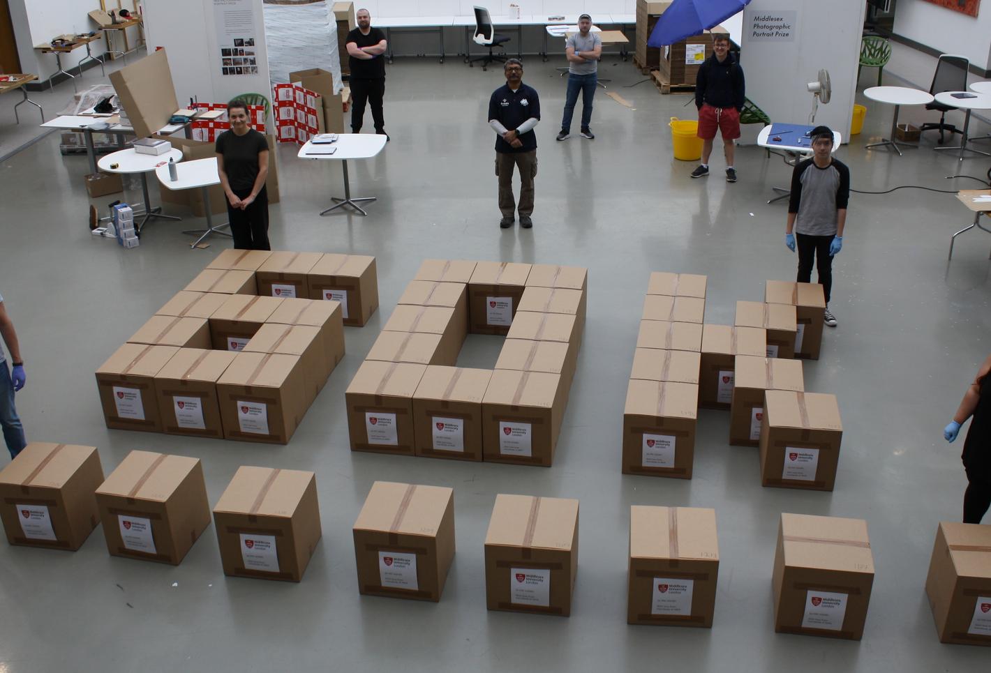 Image of people standing around boxes arranged as '60K', representing Team MDX's effort in creating 60,000 visors for the NHS in six weeks.