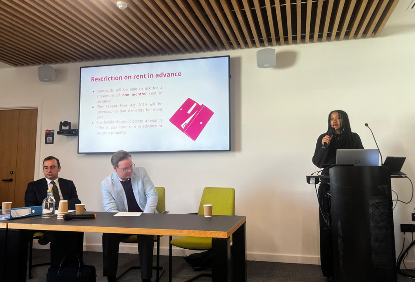 A group of three people at a lecture, one of which is presenting at a podium about the Renters' Rights Act