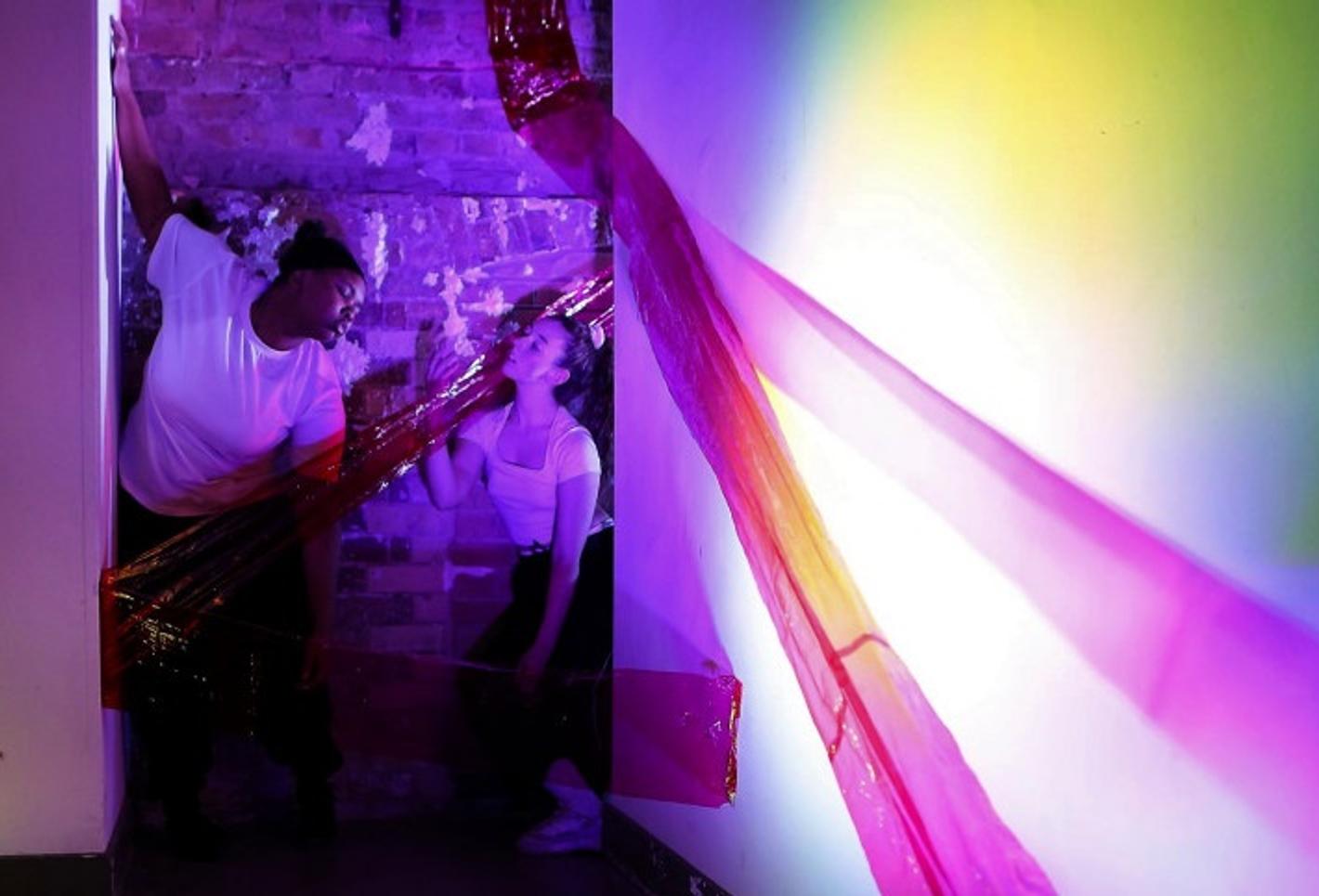 A dance image featuring two people in a room with colorful lighting.