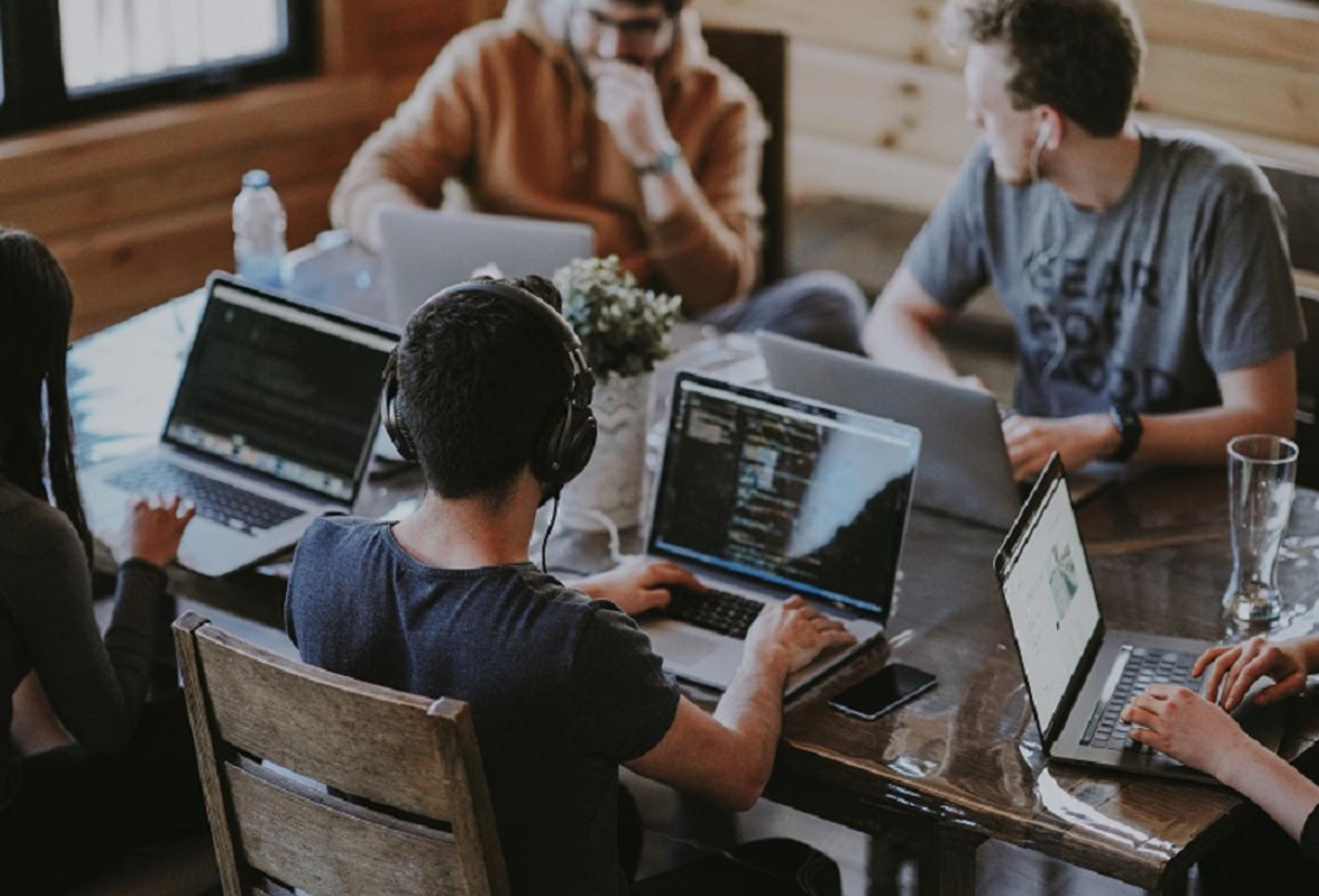 A team of professionals working together at a table, each person focused on their laptop screens