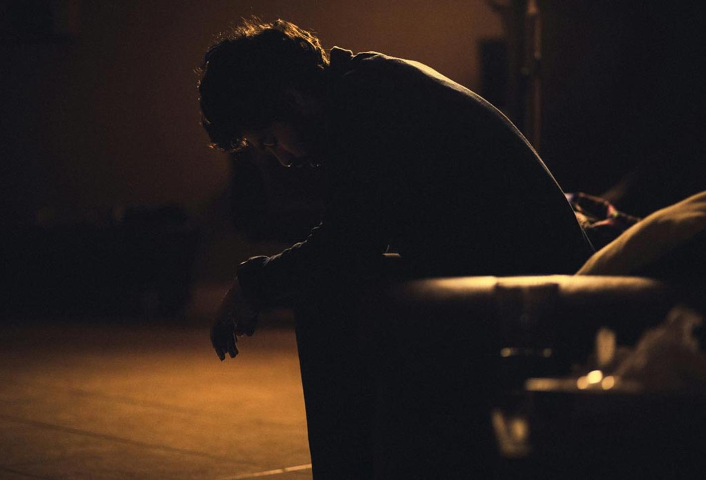 Male sitting in a dark room looking at the floor