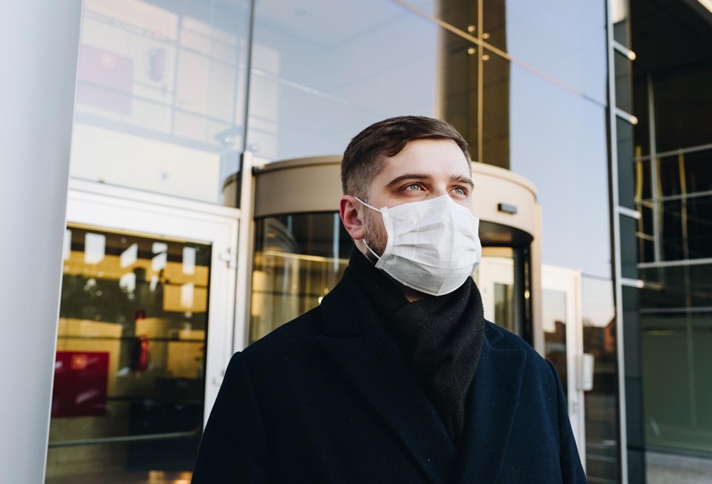 An individual wearing a face mask with a building in the background.