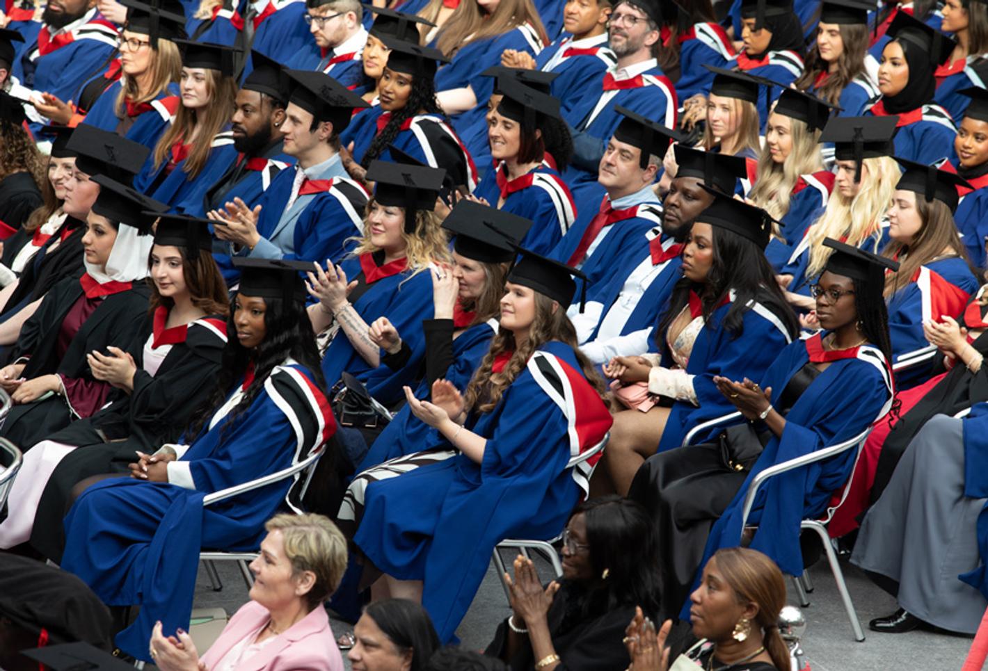 A crowd of graduating students sitting in their graduation robes and mortar boards