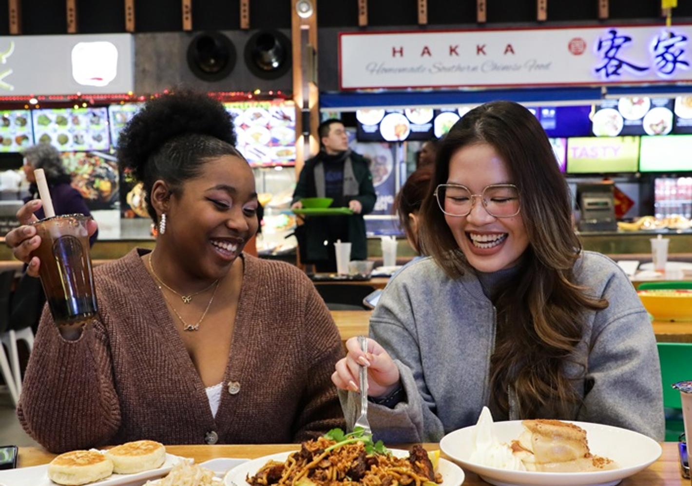 Two laughing students eating from a plate of food at Bang Bang food hall