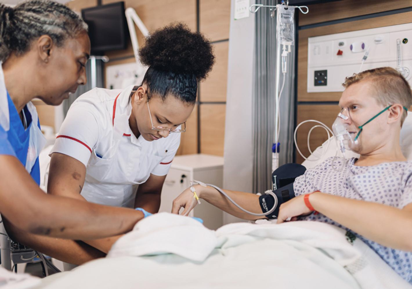 Two nurses attending to a patient who is lying in a hospital bed