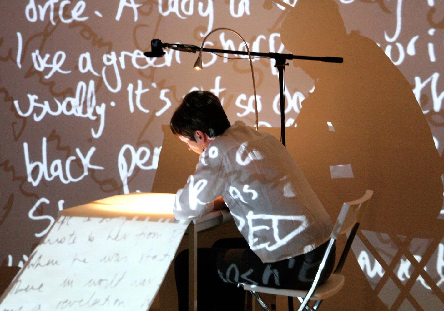 A person sat at a table writing with the words casting shadows on the wall
