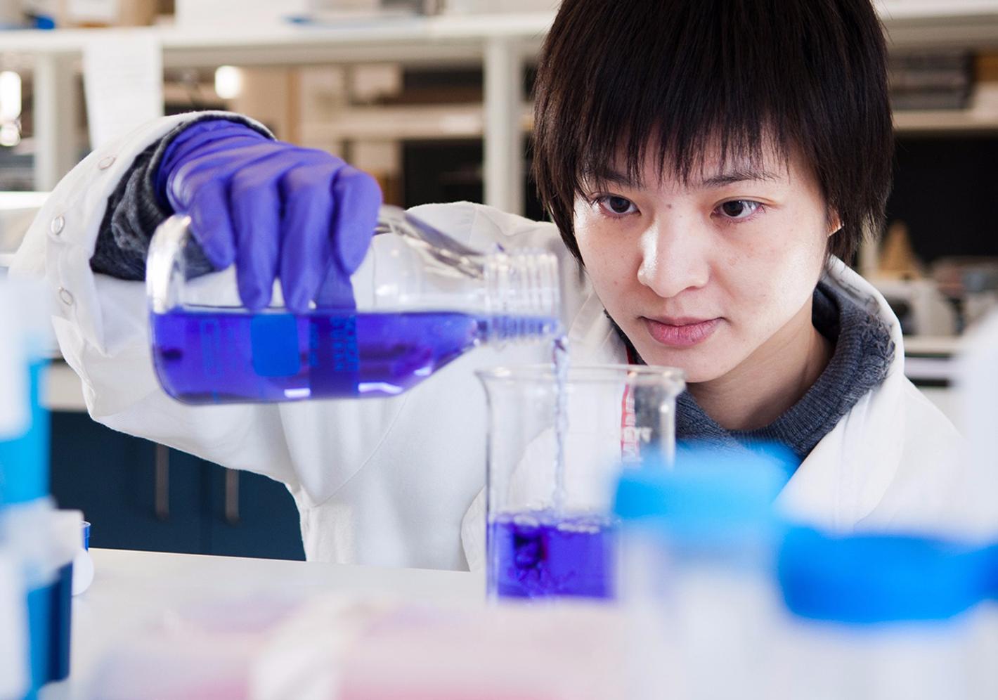 Female student in white lab coat prepares a liquid experiment in the lab at middlesex university