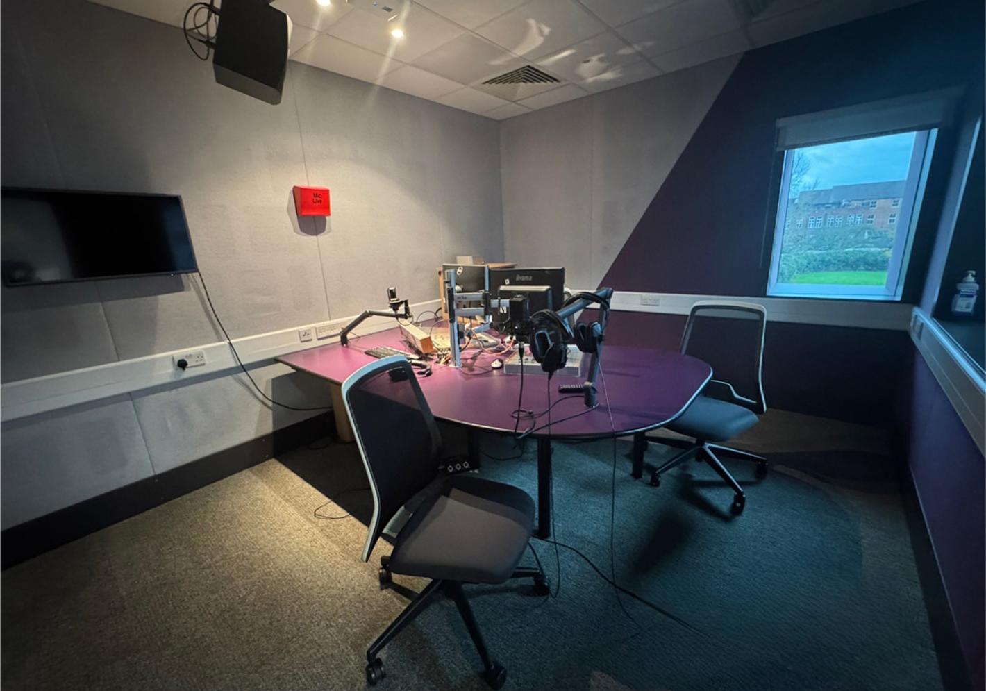 An empty audio recording studio with desks, chairs and microphones