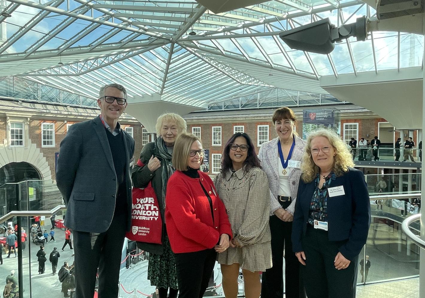 A group of adults look at the camera whilst standing on a balcony