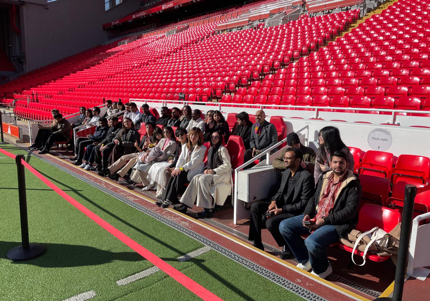 A group of people posing for a photo at the Kop End of Anfield, Liverpool FC's stadium