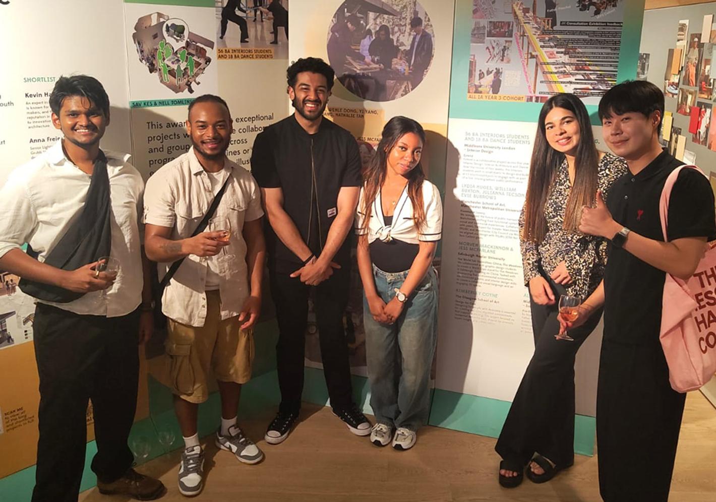 Students stand in front of posters of their designs that won awards.