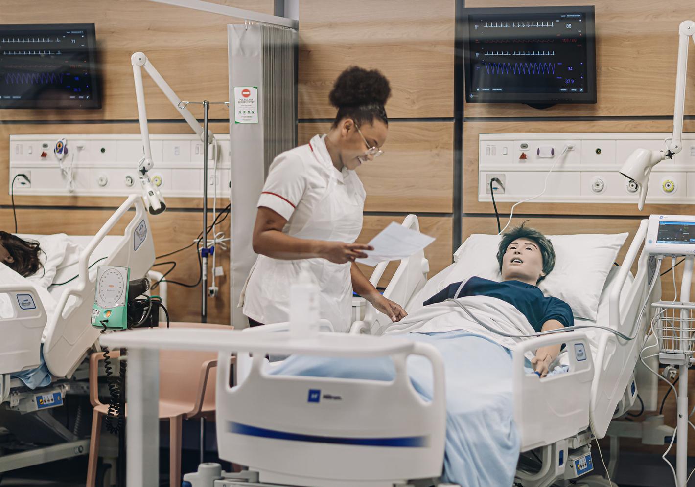 A nurse stands next to a dummy in a hospital bed