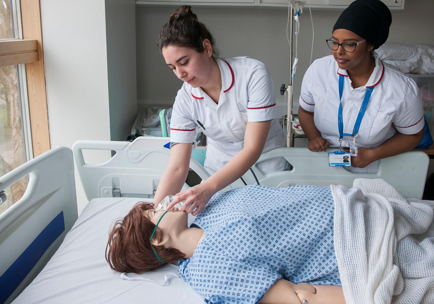 student midwife works with a pregnant dummy while teacher watches on