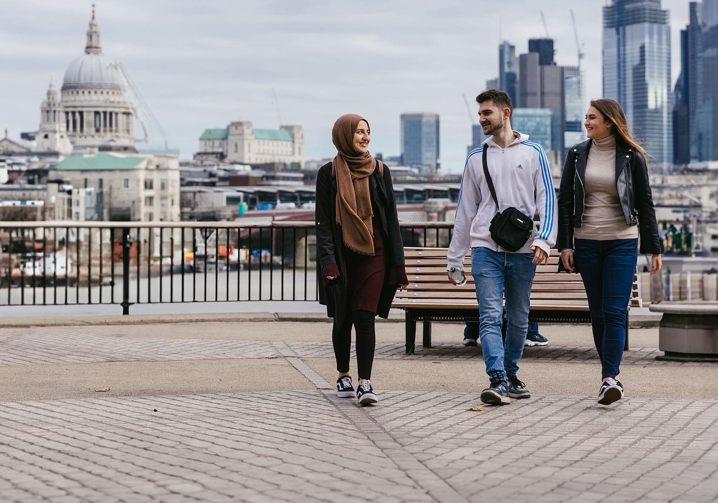 3 middlesex university students walk along the thames with st pauls in the background