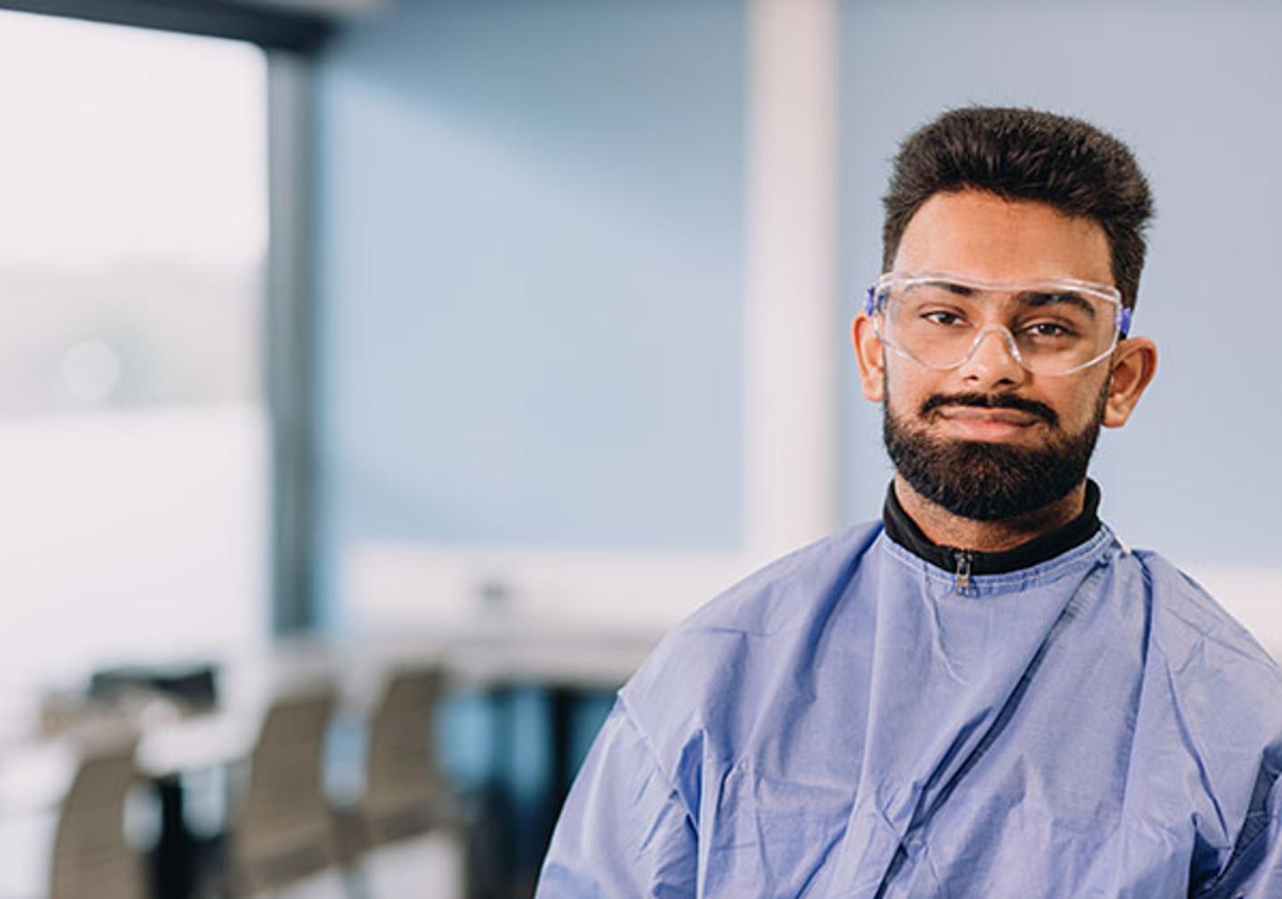 student poses in lab smock and goggles