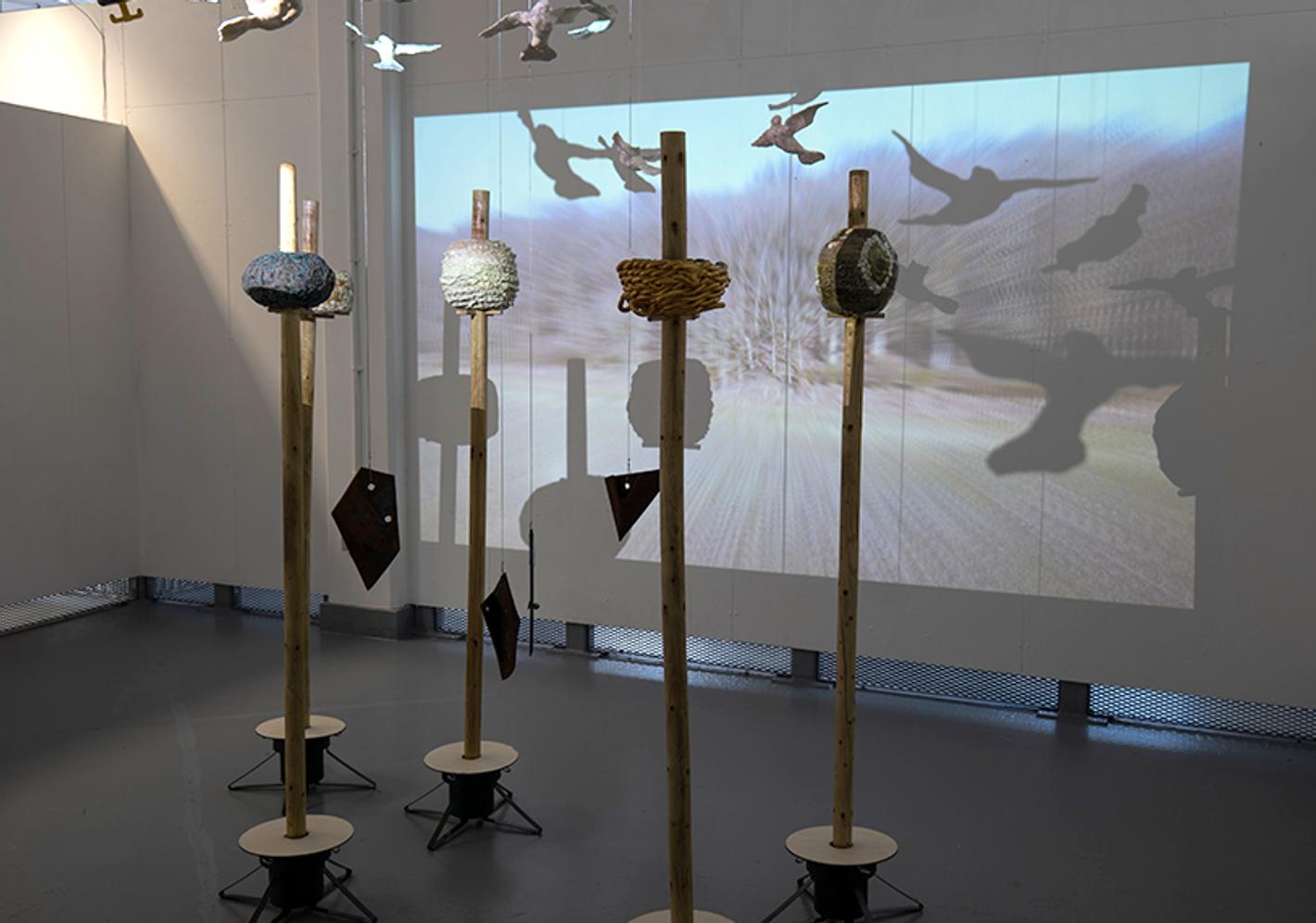 Fine Art BA student installation with sculpted poles and a bird projection backdrop
