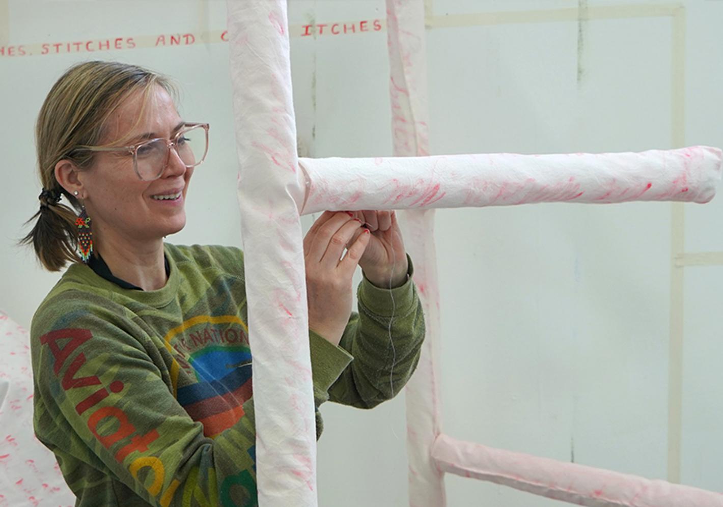 An artist sewing fabric around a sculptural frame