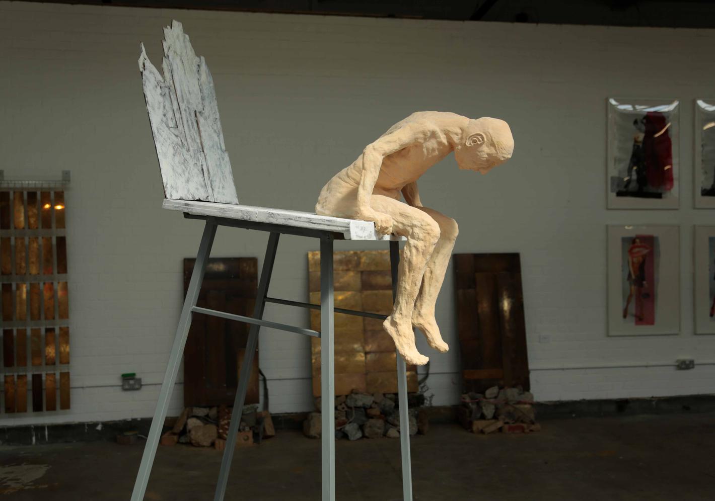 A sculpture of a man leaning over at the end of a very tall chair