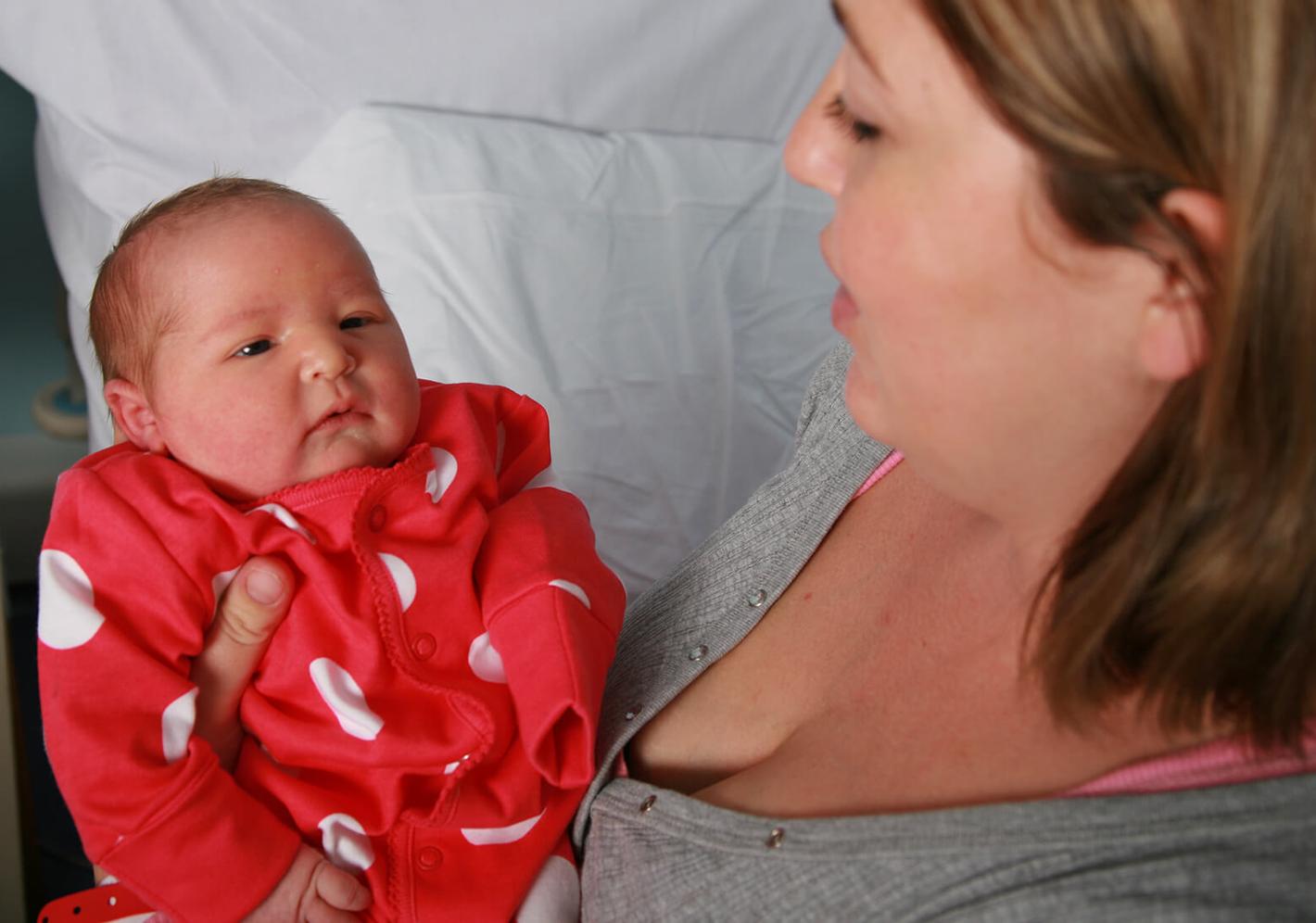 Mother holding baby in red spotted baby grow
