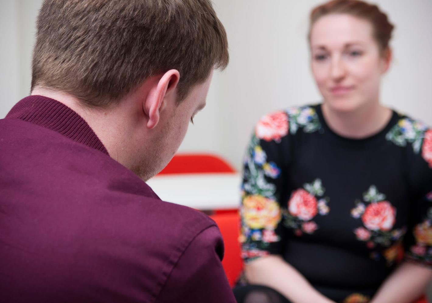 A man and woman sitting in an office, engaged in a professional discussion. Both individuals appear focused and attentive.