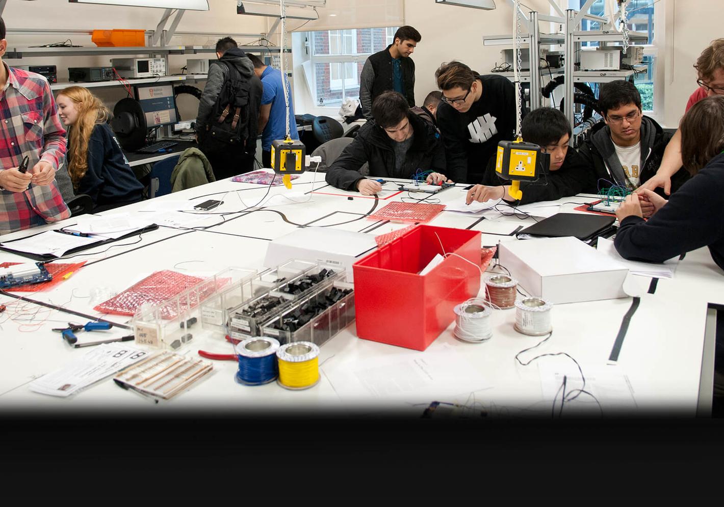 A diverse group of individuals engaged in electronics work in a classroom as part of their Foundation Year in Computing and Engineering.