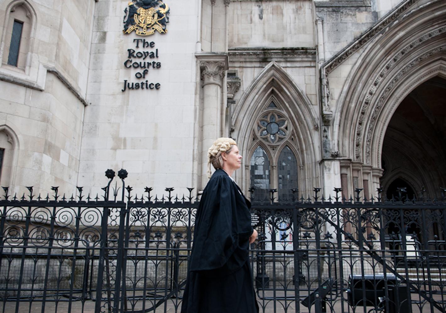 A law student in a wig and gown walking beside the Royal Court of Justice