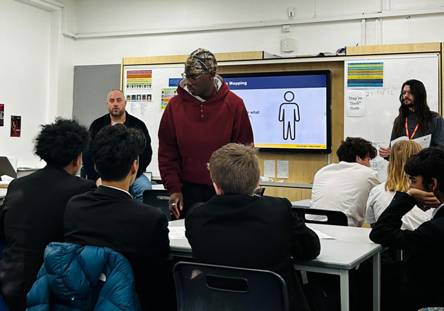 Male school pupils in a classroom talking to an adult male delivering a workshop