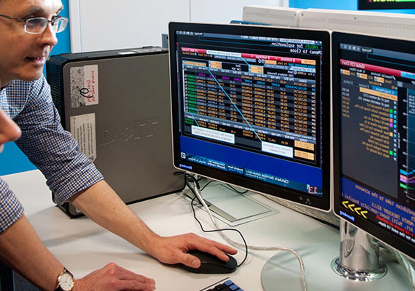 Two individuals analyzing stock market data on computer screens in an accounting and finance setting.