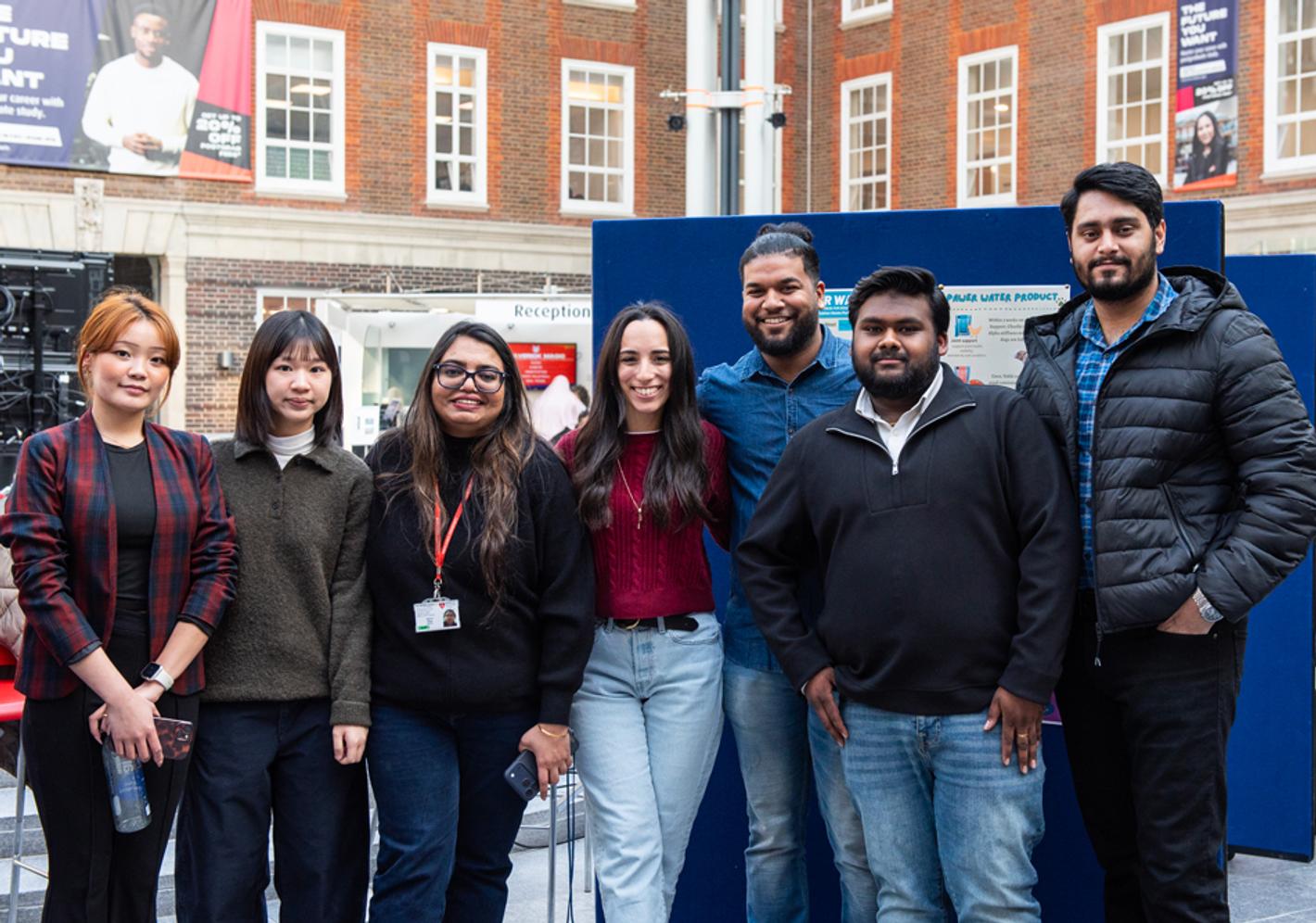 A group of students standing inside a university building, posing for the camera