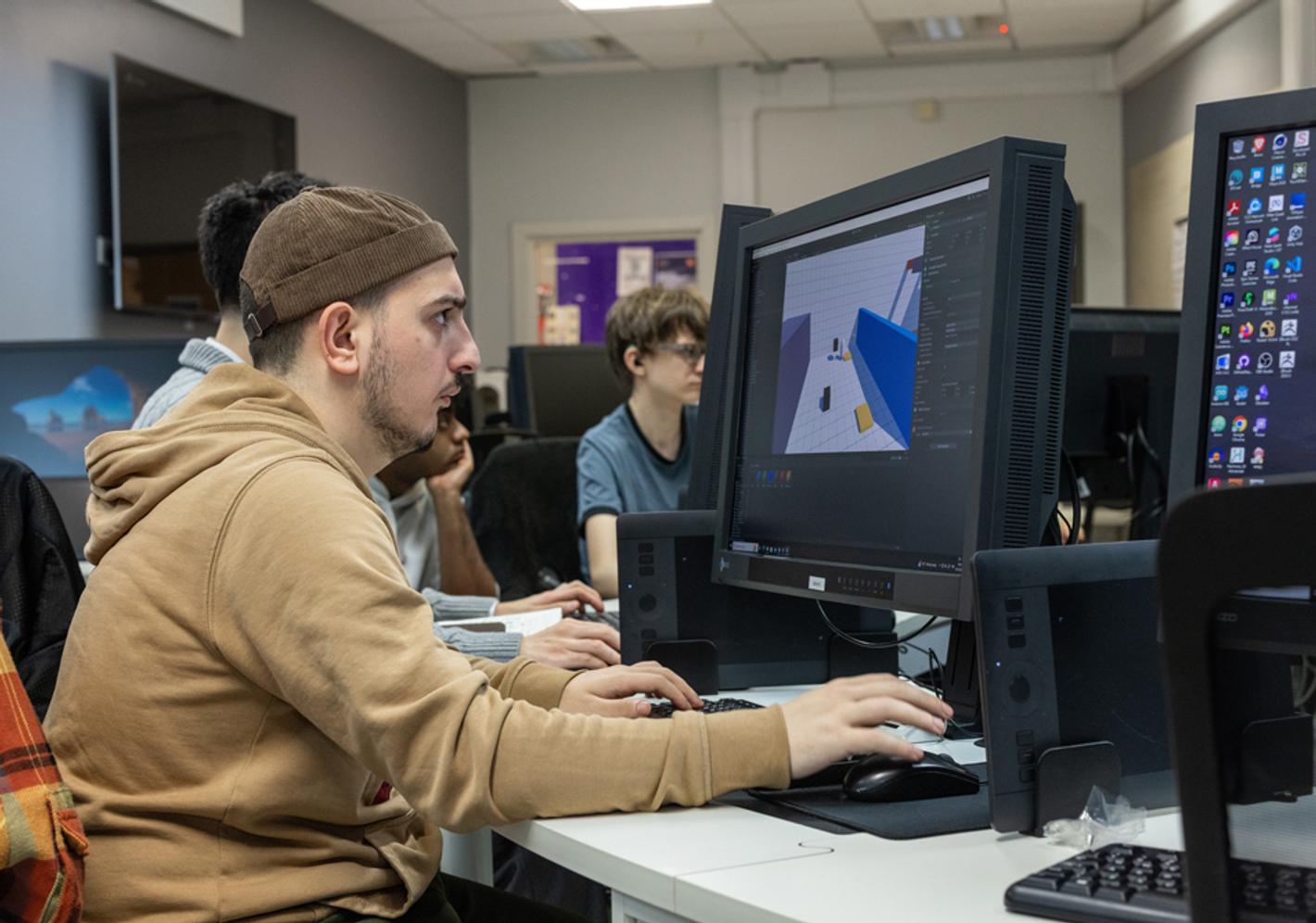 A student wearing a hat working at a computer terminal