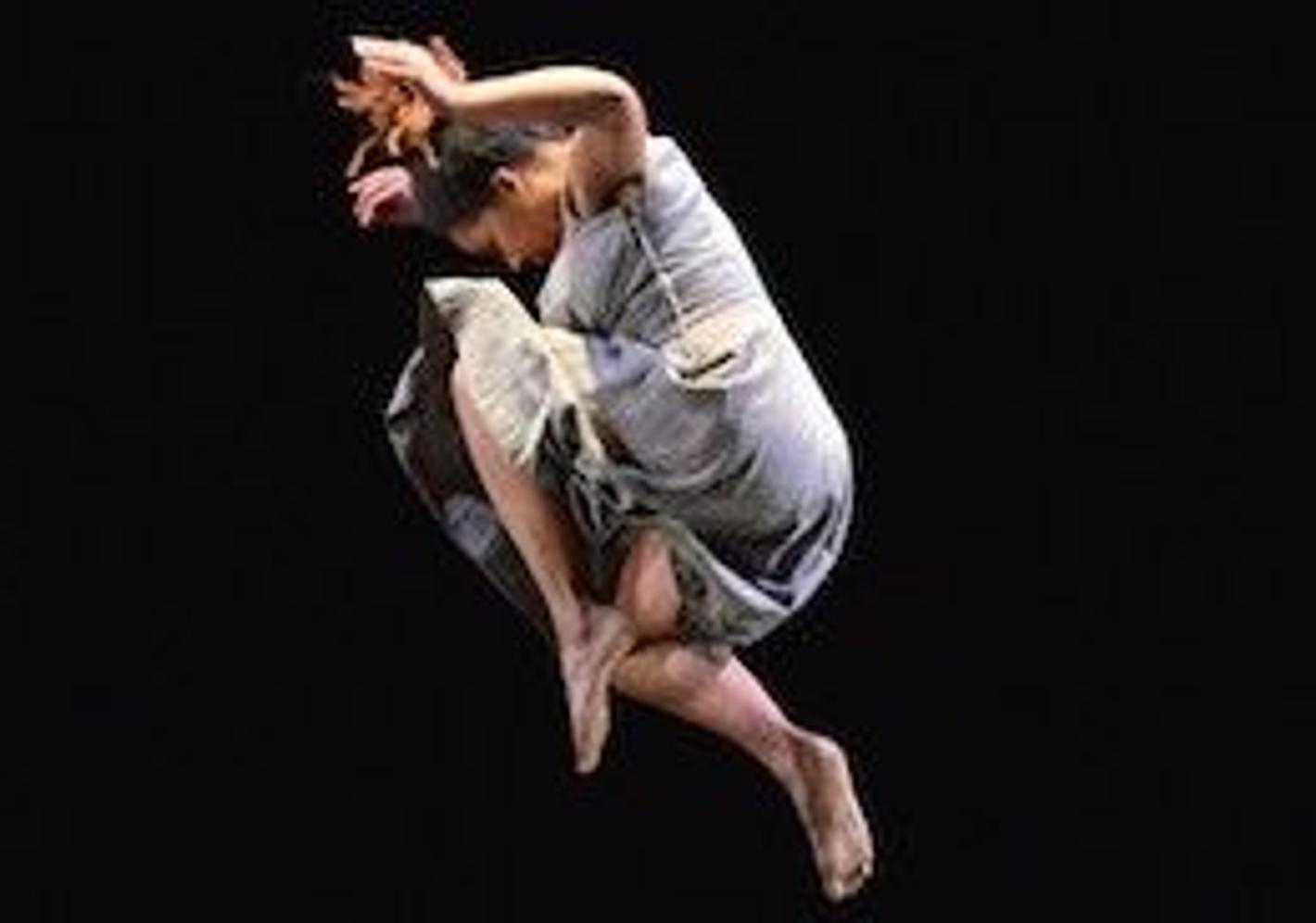 A woman joyfully leaps into the air, wearing a flowing dress that gracefully follows her movements.