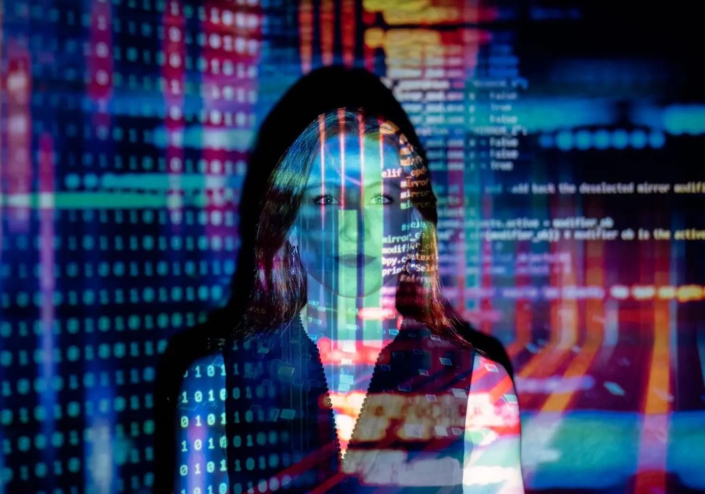 Woman facing the camera with a reflection of a coding screen projected across her face.