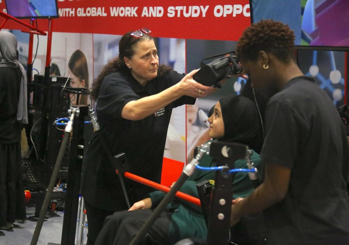A woman helps a school student put on a helmet for a rollercoaster simulator