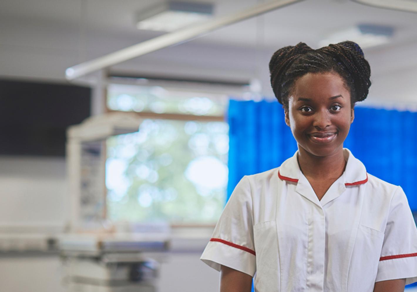 A nurse in a hospital ward smiles directly at the camera