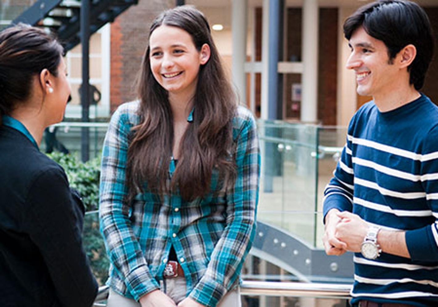 Three students engaged in conversation in a well-lit indoor space.