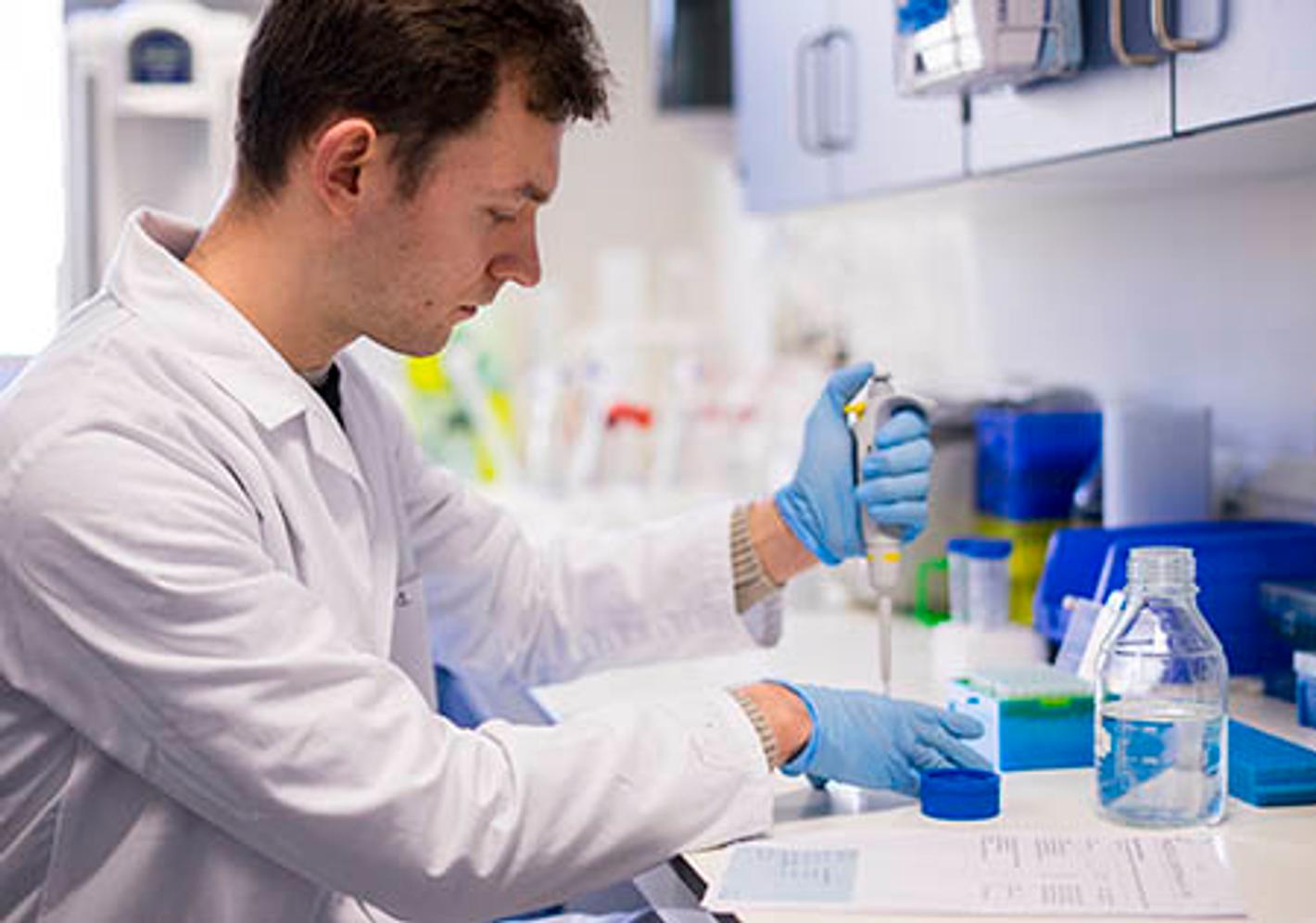 male student in white coat and wearing gloves prepares a sample for analysis
