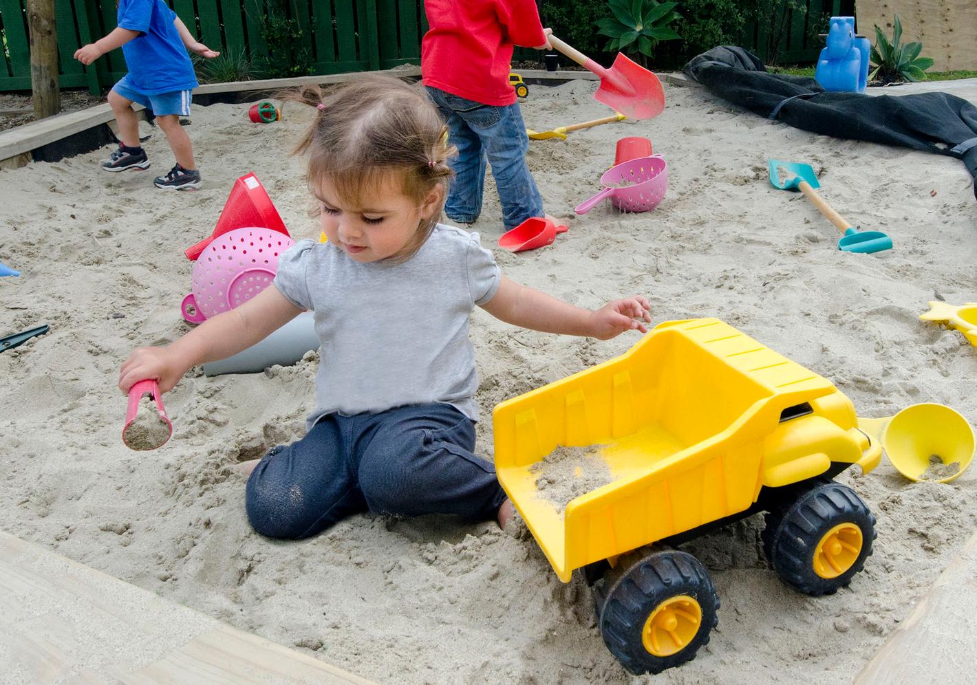 small child plays in sandpit with toy truck