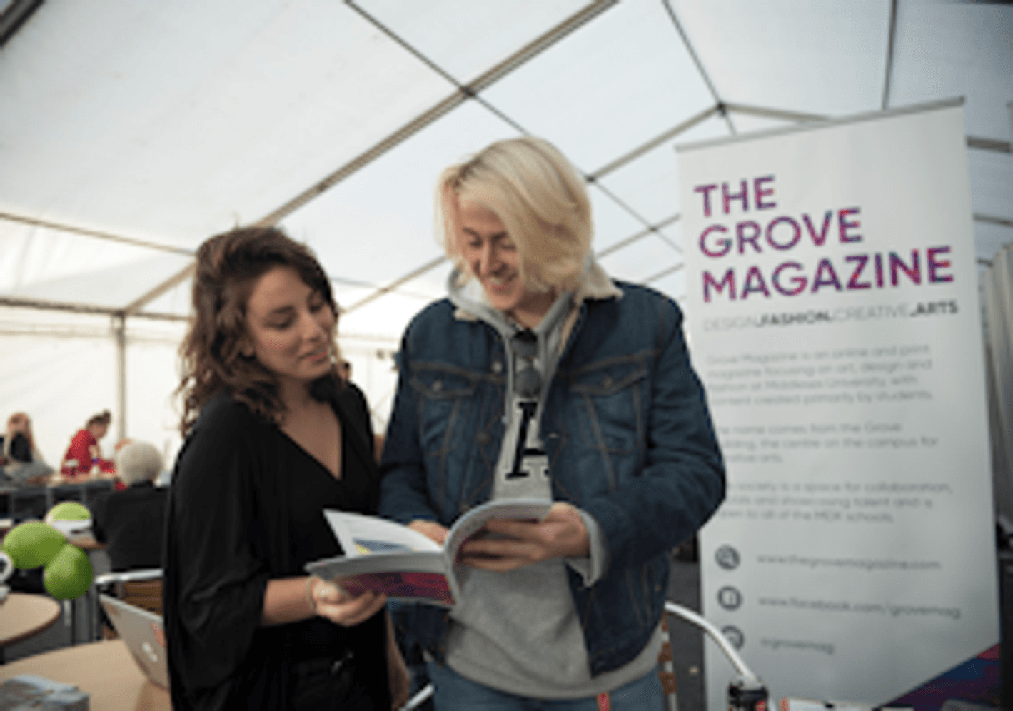 Two individuals reading a magazine inside a tent. Encouraging involvement in university THE GROVEmagazines.