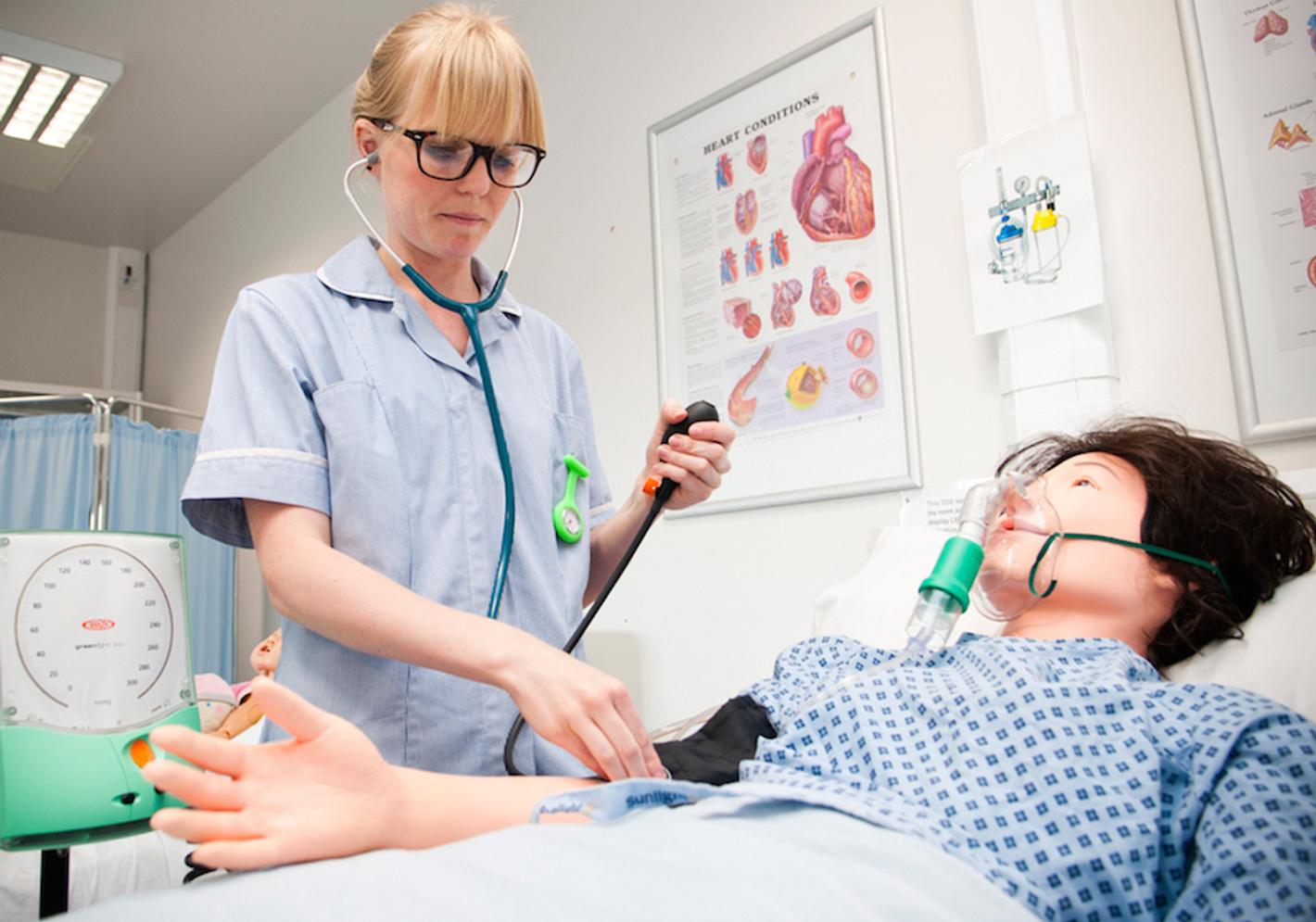 Image of a woman in a blue shirt, practicing nursing and midwifery skills in a lab setting.