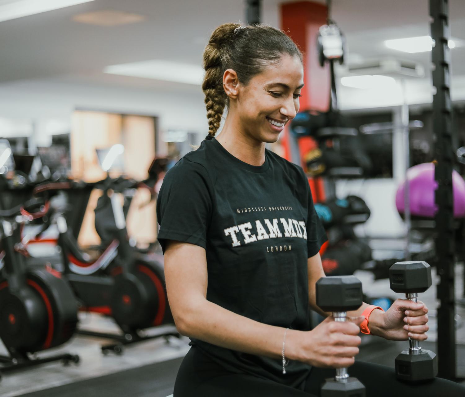 A gym goer smiling with a dumbell in their hand, in the Fitness Pod.