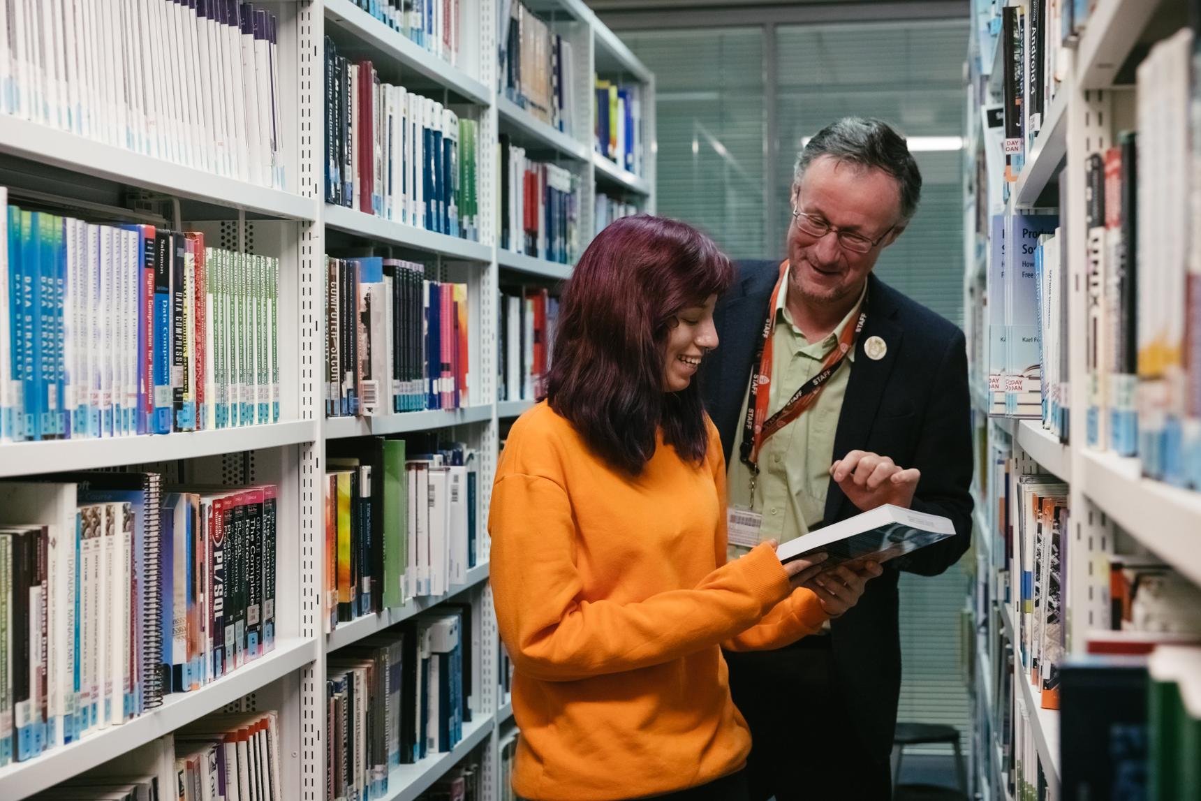 A man and woman in a library, engrossed in books.