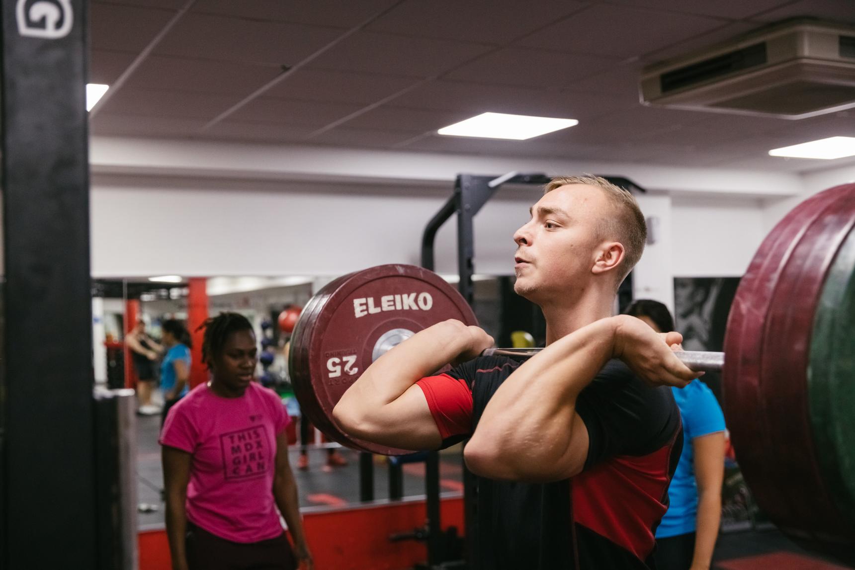 A man performing weightlifting exercise with a barbell at a gym.