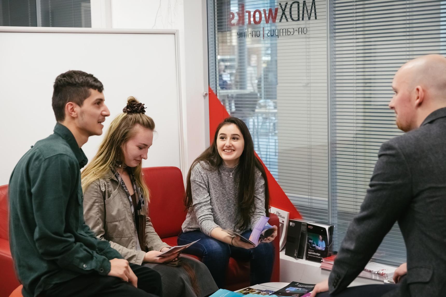 Four students engaged in a lively conversation while seated in a room.