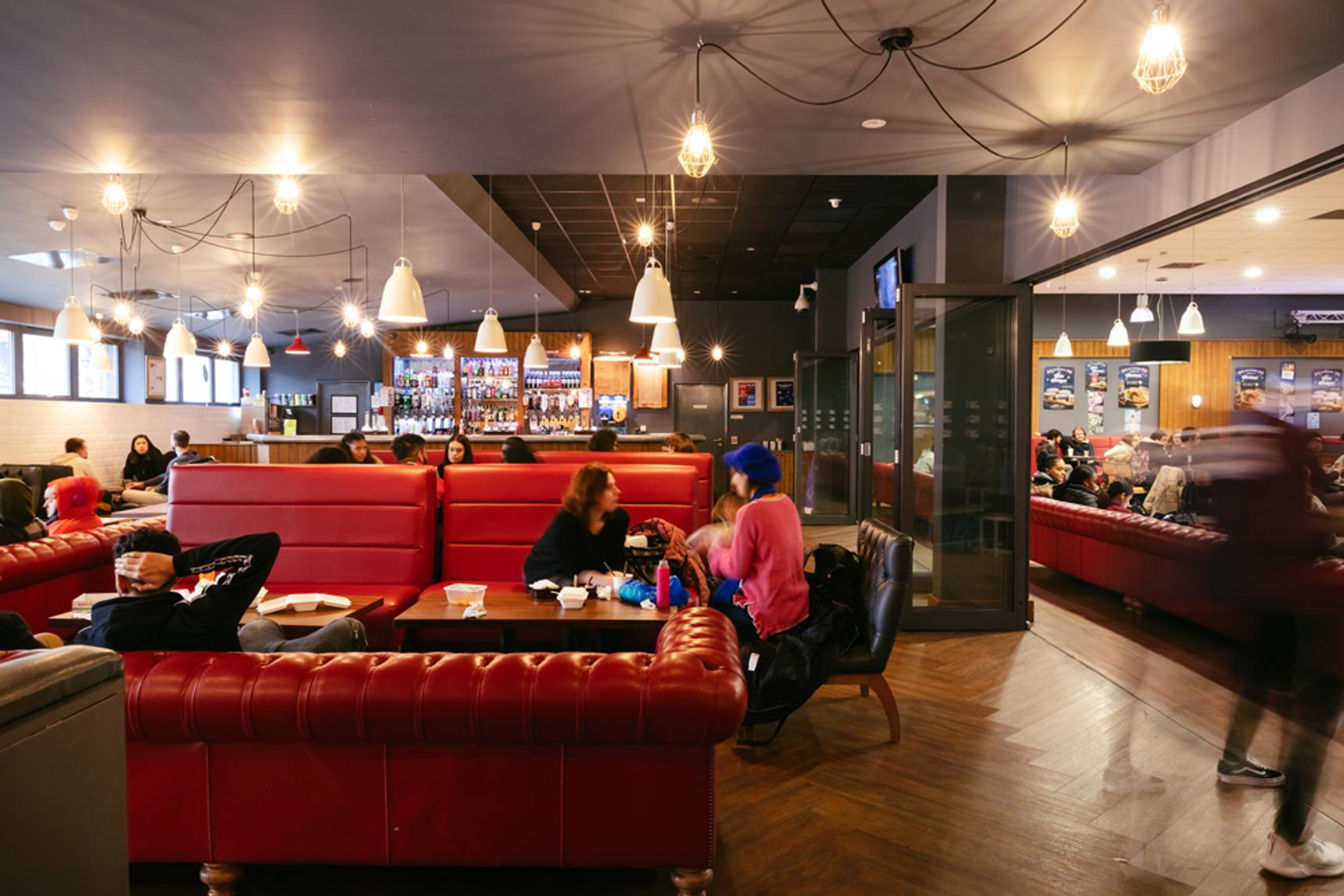 Interior of a bar and seating area in MDX House at Middlesex University, with blurred figures sitting and walking past