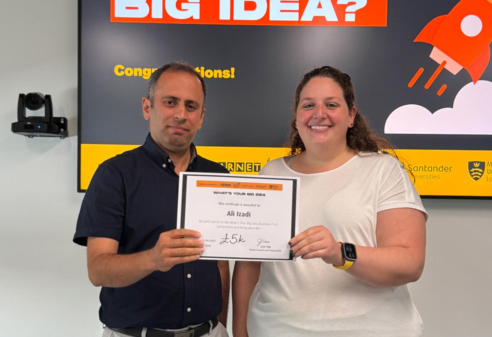 A man in a blue shirt and woman in a white top stand both holding a certificate