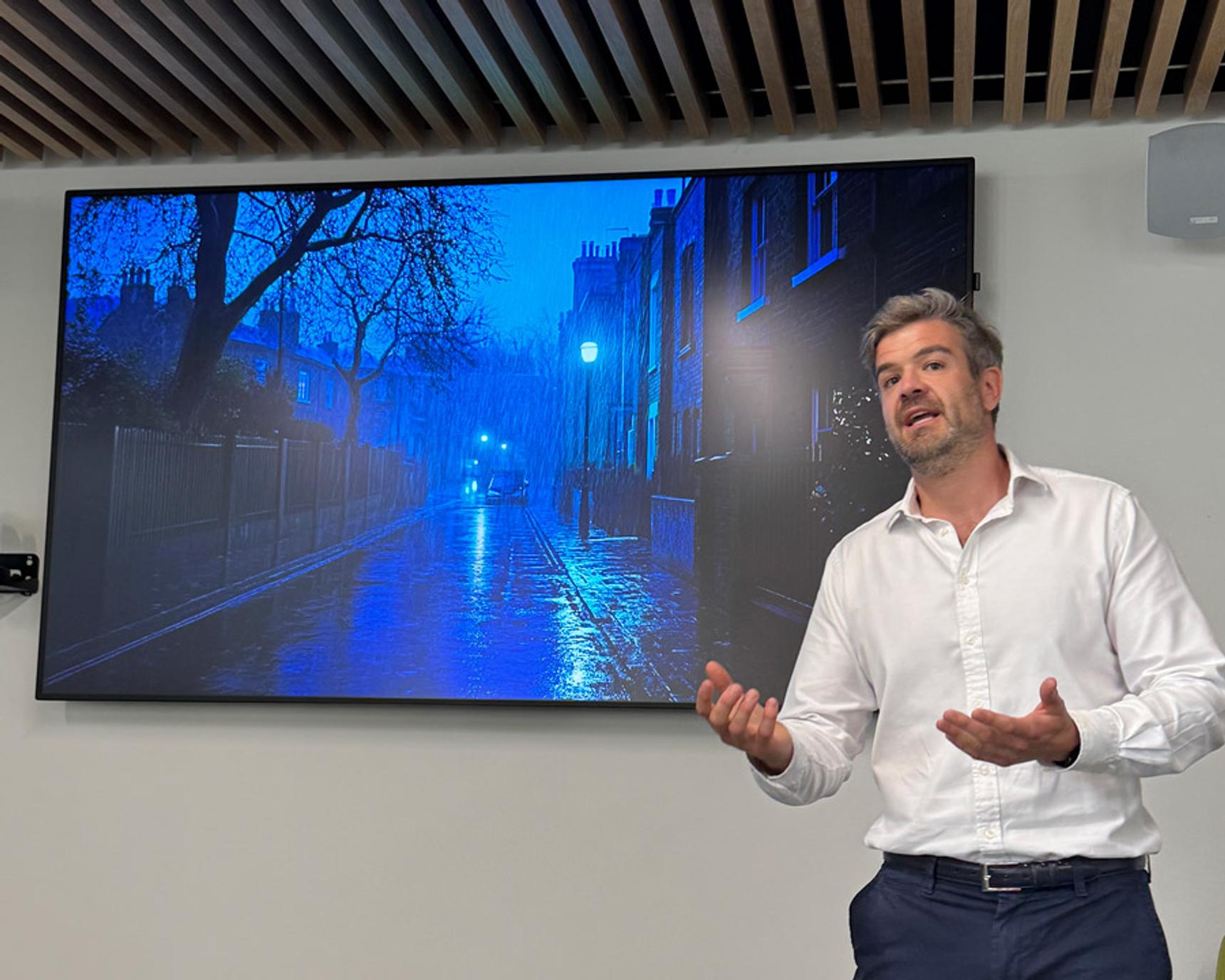 A MDX MBA student in a white shirt gestures in front of a screen with a photograph in blue tones