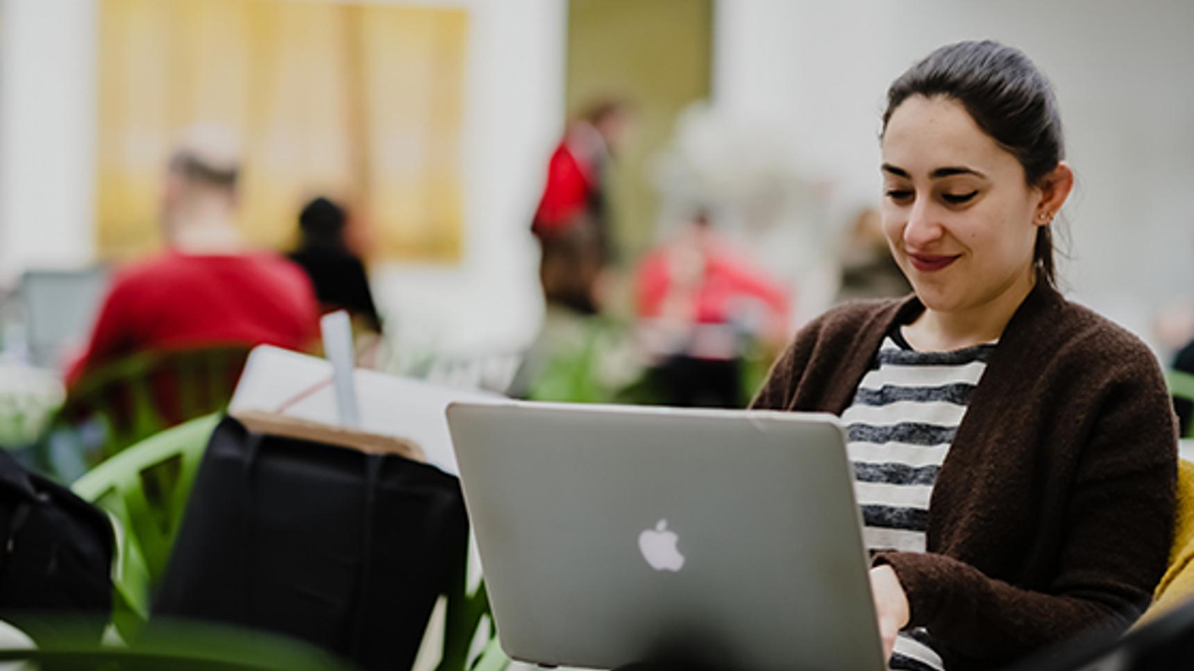 A woman sitting on a chair with her laptop, focused on her work.