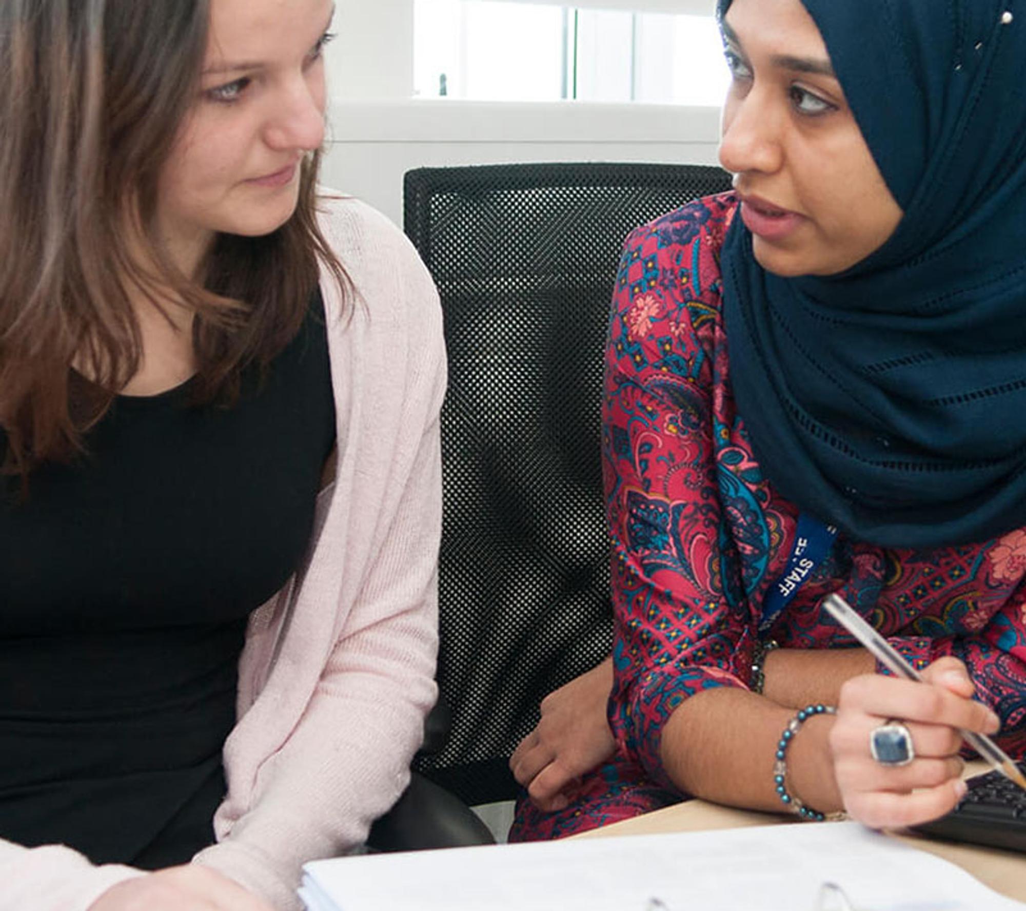 one woman in a headscarf and another woman sat down in a classroom